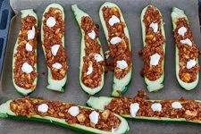 Zucchinihälften mit Hackfleischfüllung und Crème fraîche vor dem Überbacken