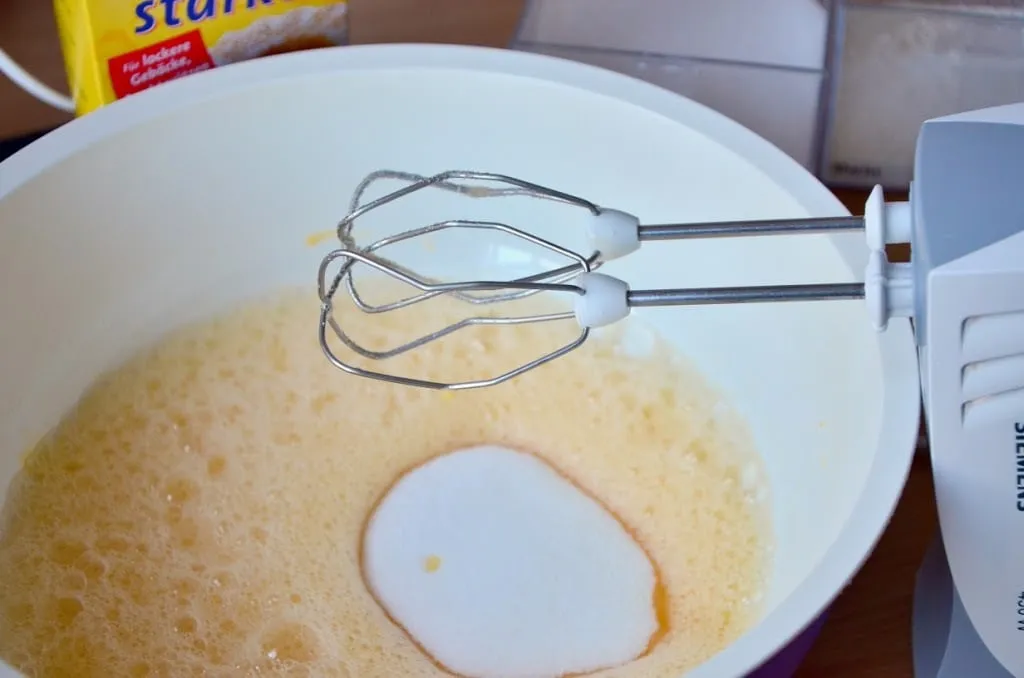 Zucker und Vanillezucker zum schaumigen Eier-Wasser-Gemisch rühren für den Biskuitboden