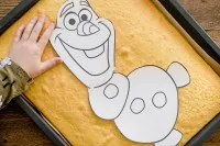 Zuschnitt des Olaf-Kuchens mit einem scharfen Messer entlang der Papierschablone, für eine exakte Form.