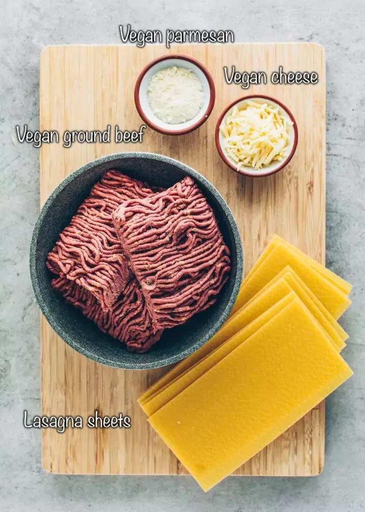 Zutaten für Lasagne: Veganes Hackfleisch, Lasagneblätter, veganer Reibekäse und veganer Parmesan auf einer hellen Unterlage.