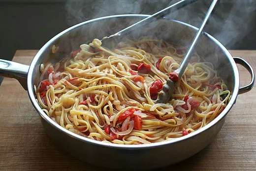 Zutaten für One-Pan Pasta: Linguine, Tomaten, Zwiebeln, Knoblauch und Basilikum in einer großen Pfanne