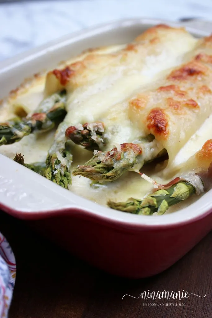 Zutaten für Spargel-Lasagne-Röllchen: Frischer grüner Spargel, Lasagneblätter, Schinken und Käse auf einer Holzoberfläche