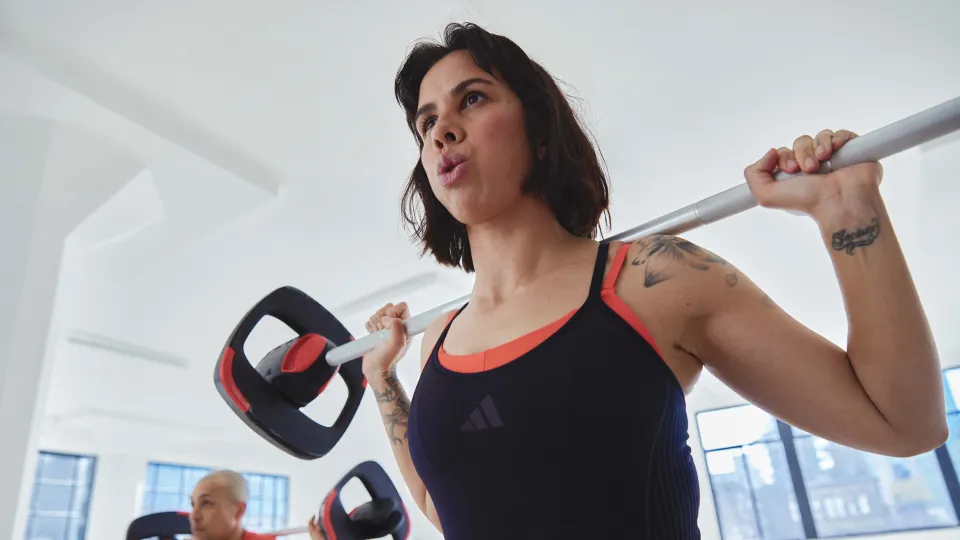 Zwei Frauen beim Bodypump-Training, die Brustpresse mit Langhanteln auf einer Bank ausführen, als Beispiel für die vielfältigen Übungen im Kurs.