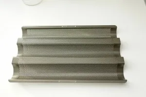 Zwei geformte Baguette-Teigstränge ruhen in einer speziellen perforierten Baguette-Backform, bereit zum letzten Gehen und Backen.