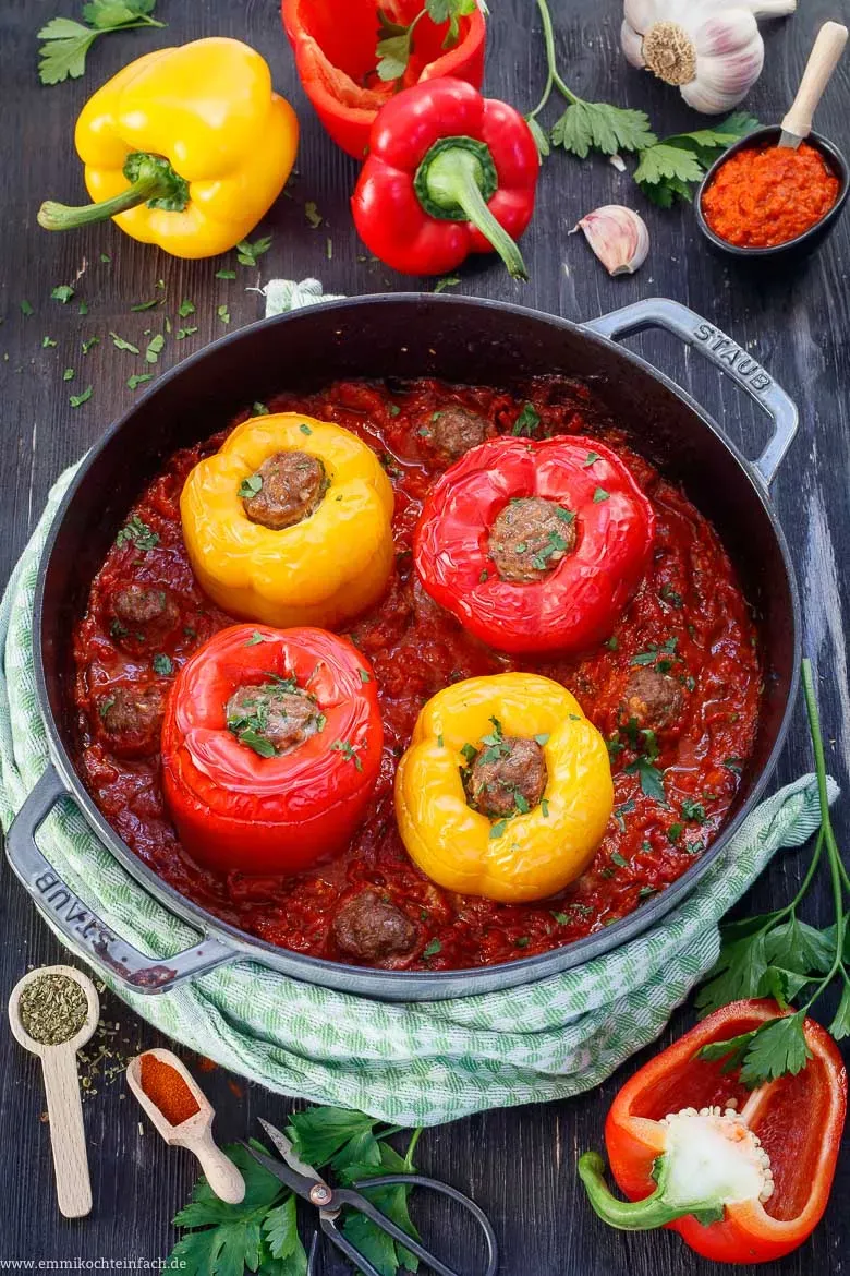 Zwei gefüllte Paprikaschoten mit Hackfleisch in einem Topf, bereit für den Backofen, mit frischen Kräutern dekoriert