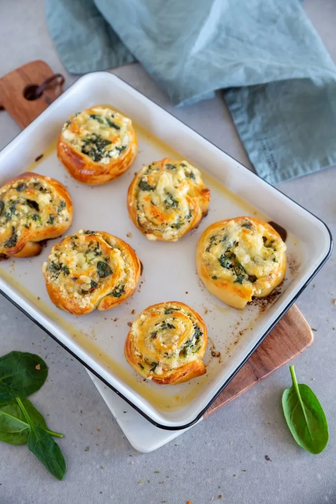 Zwei goldbraune Feta-Spinat-Pizzaschnecken appetitlich auf einem Holzbrett angerichtet