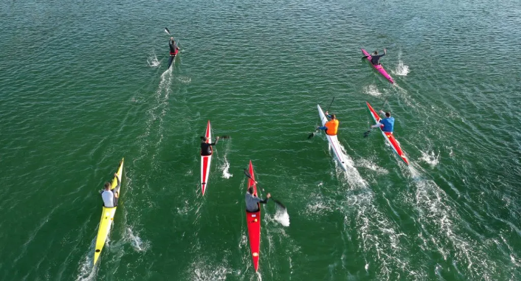 Zwei Kanufahrer in Rennkanus auf einem ruhigen Fluss, bereit für den Start.
