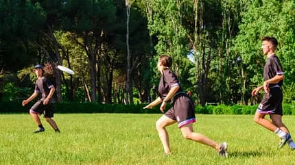 Zwei Männer und eine Frau in Sportkleidung spielen auf dem Rasen mit einer Frisbee.