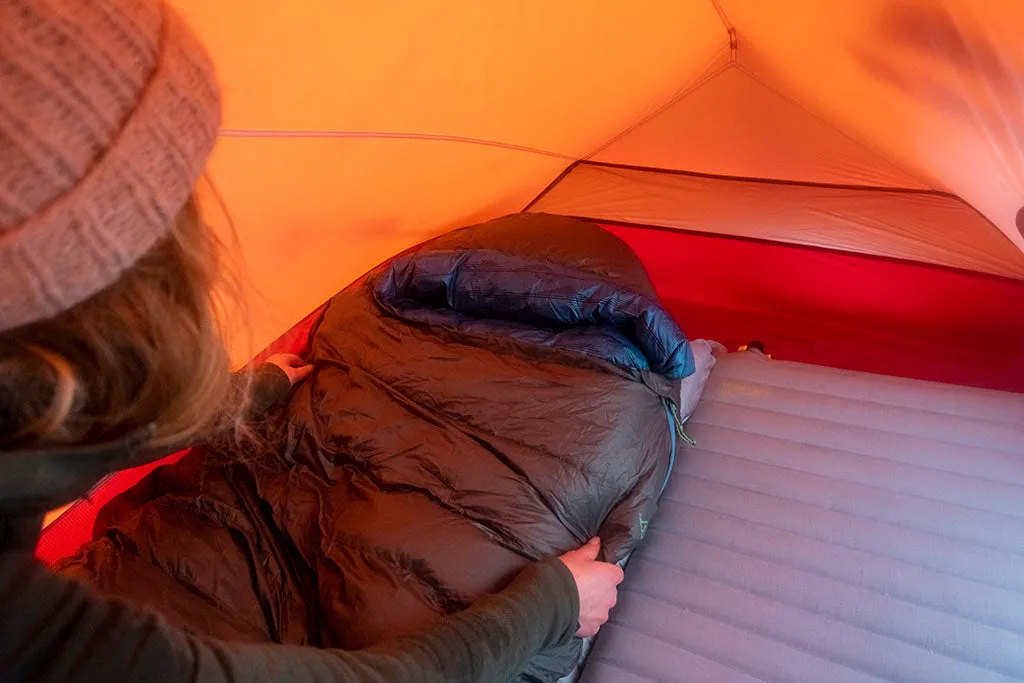 Zwei Personen sitzen entspannt im Zelt und lesen ein Buch, mit Blick auf schneebedeckte Berge