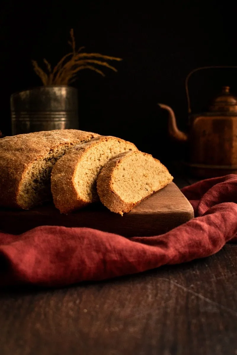 Zwei Scheiben herzhaftes Roggenbrot neben dem restlichen Laib auf einem Holzschneidebrett.
