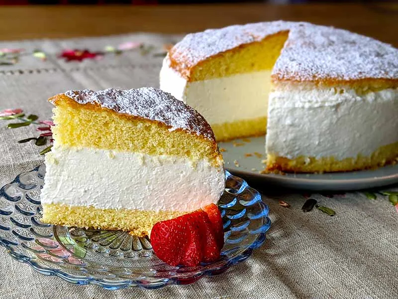 Zwei Scheiben Käse-Sahne-Torte auf einem Teller, mit weiteren Stücken im Hintergrund