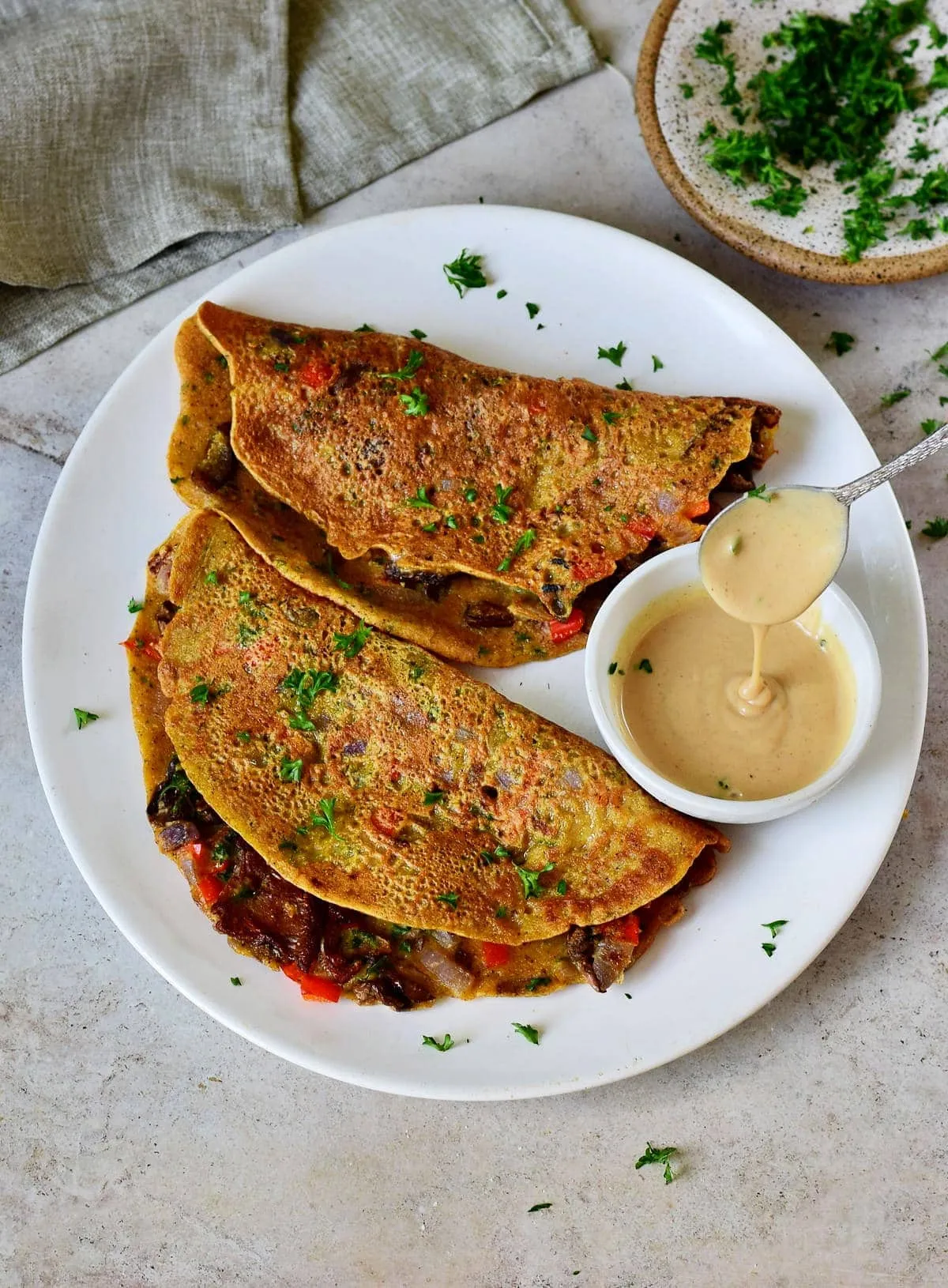 Zwei vegane Omeletts mit Pilzen und Gemüse auf einem weißen Teller mit cremigem Dressing, ein köstliches eifreies Mittagessen.