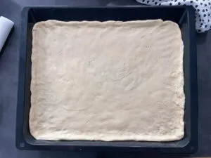 Zwiebelkuchenteig, der auf einem Backblech ausgerollt ist und bereit ist, belegt zu werden