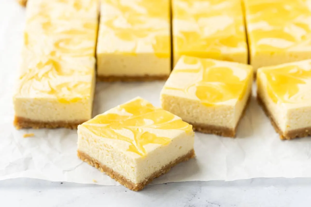 Appetitliche Meyer-Zitronen-Käsekuchen-Riegel mit leuchtendem Zitronen-Curd auf Backpapier, bereit zum Genießen.