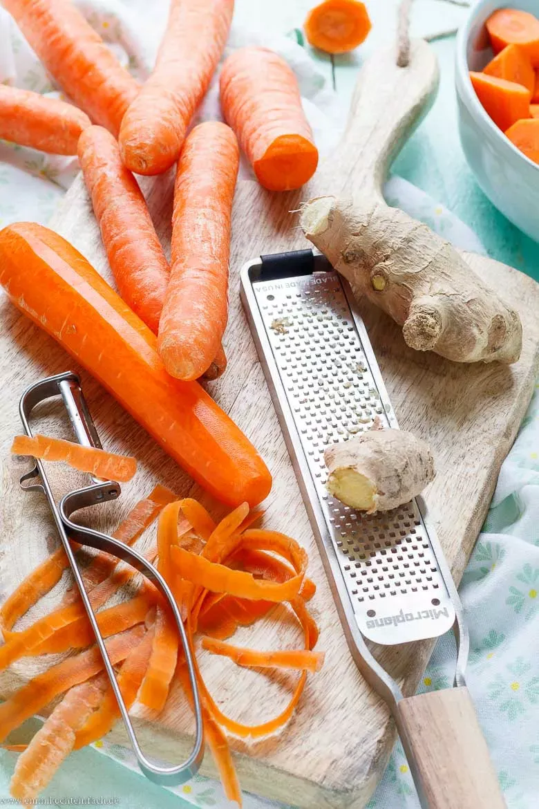 Auswahl frischer Zutaten wie Möhren, Ingwer, Zwiebel und Orangensaft für die Möhrensuppe
