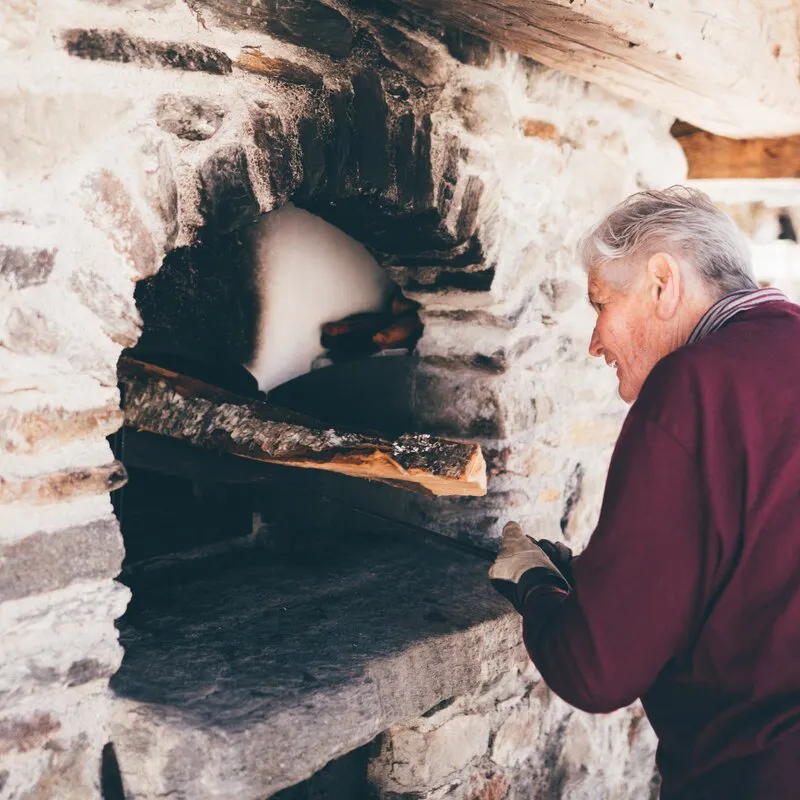 Bäuerin legt Holzscheite in einen traditionellen Bauernofen.