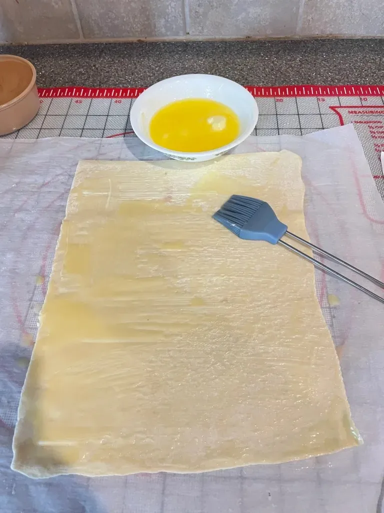 Blätterteig auf Backpapier ausgerollt und mit Butter bestrichen