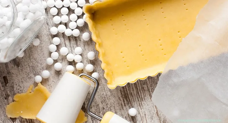 Blindbacken eines Mürbeteigbodens mit Backpapier und Hülsenfrüchten