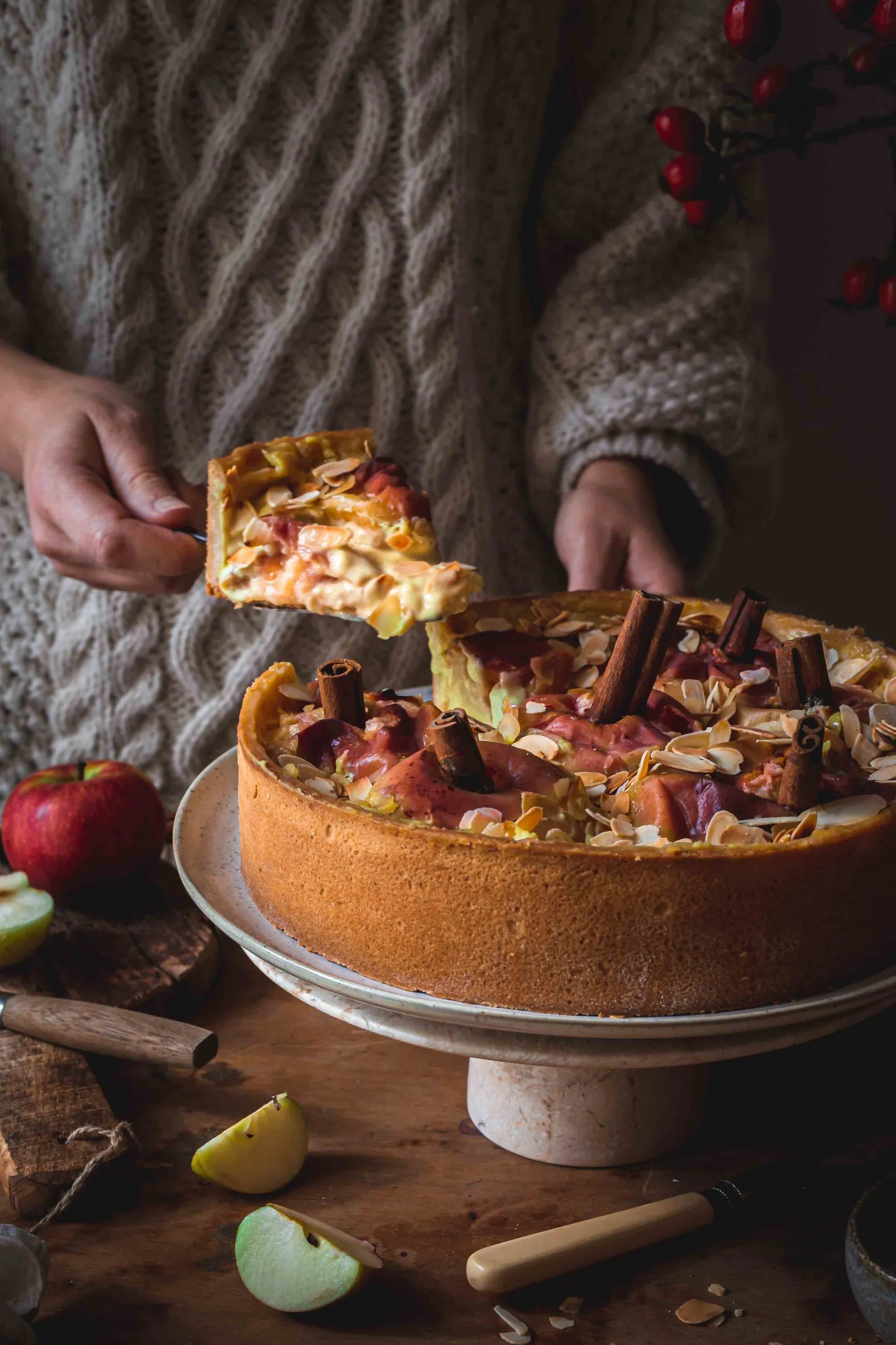 Bratapfelkuchen mit Zimtstangen verziert, aus der Springform genommen und auf einem Kuchenständer