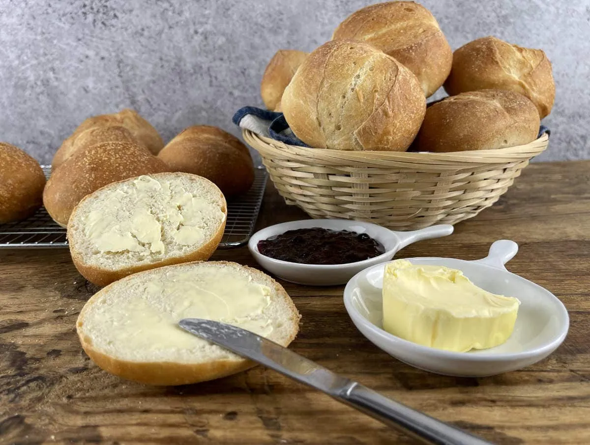Brötchen in a basket with butter and jam with a buttered split roll.