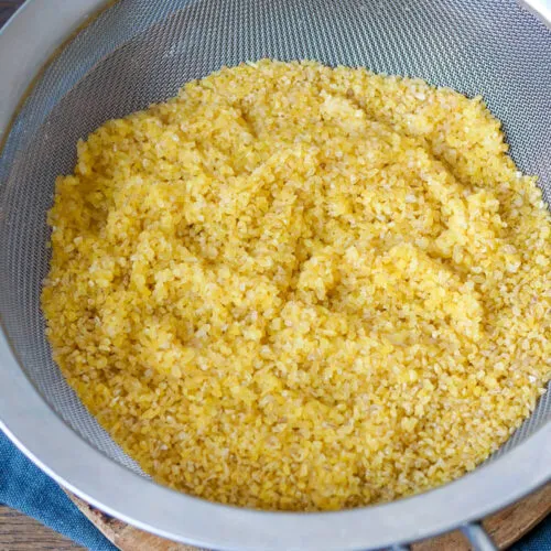 Bulgur wird in einem Sieb unter fließendem Wasser abgespült.