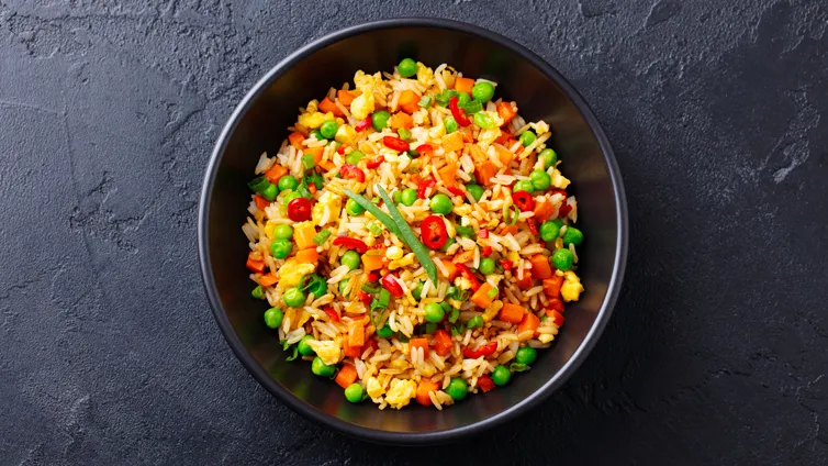 Bunte Gemüse-Reispfanne in einer Glasschale mit Reis, Karotten und grünen Erbsen.