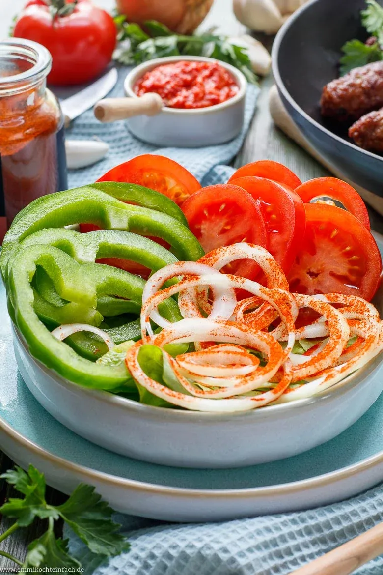 Cevapcici mit frischen Zwiebeln, Tomaten und Ajvar auf einem Teller serviert