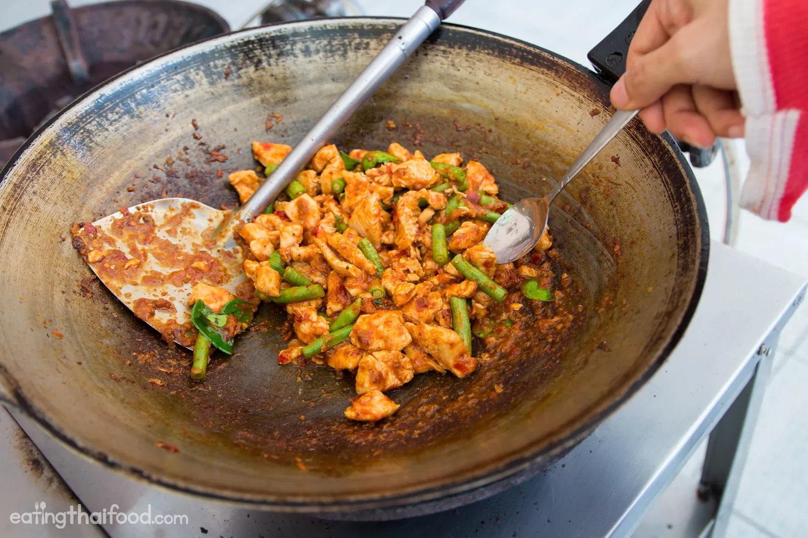 Currypaste und Hähnchenbrust beim Anbraten in der Wokpfanne