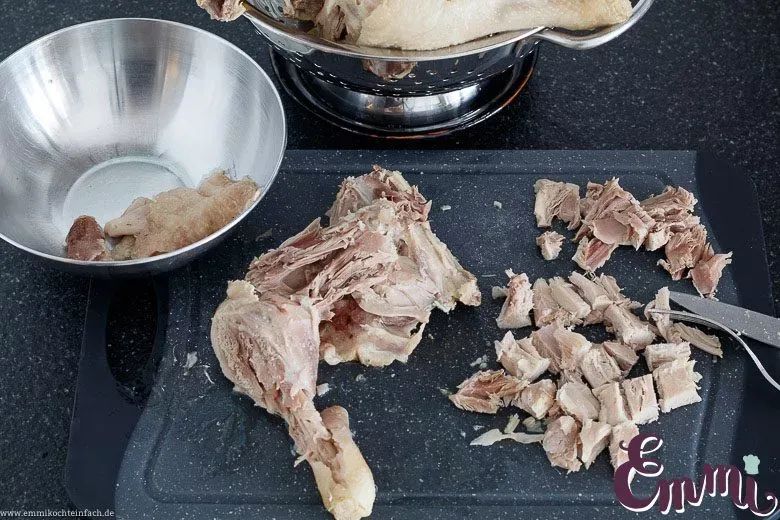 Das gekochte Suppenhuhn-Fleisch wird von den Knochen gelöst und in mundgerechte Stücke geschnitten.