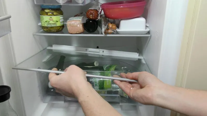 Das unterste Fach des Kühlschranks wird entfernt, um Zugang zum Ablauf zu erhalten.