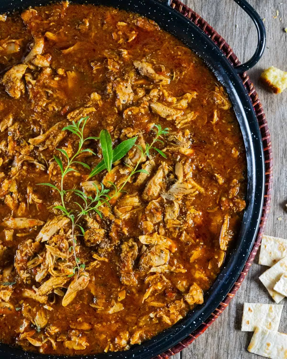 Deftige spanische Bauernessuppe in einer Paella-Pfanne, garniert mit Bohnenkraut und frischen Lorbeerblättern.
