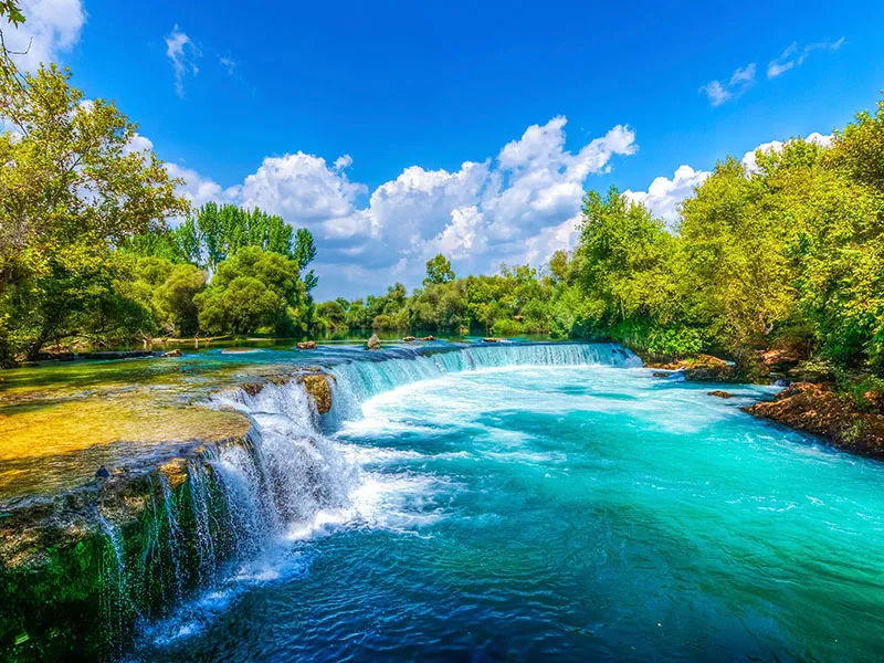 Der breite Manavgat-Wasserfall, umgeben von grüner Vegetation, mit Menschen am Ufer