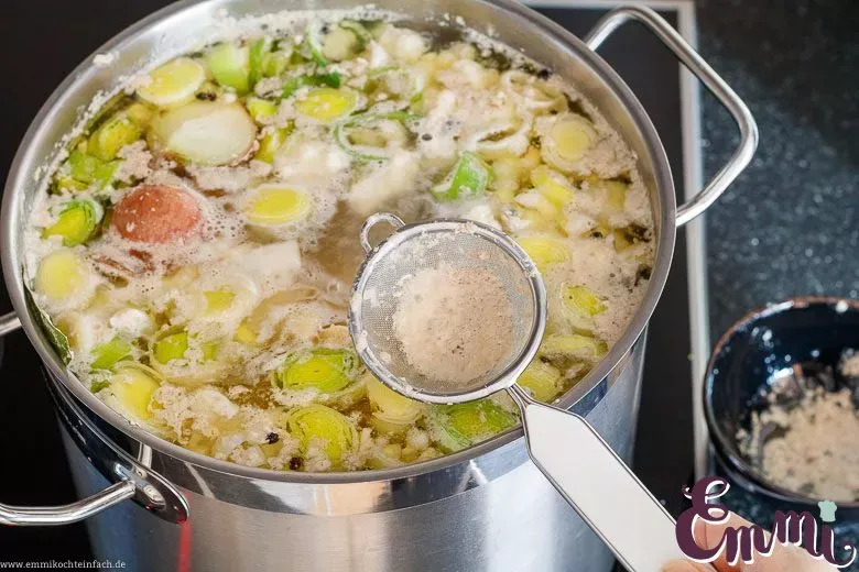 Der Schaum, der beim Kochen der Hühnersuppe entsteht, wird sorgfältig abgeschöpft, um eine klare Brühe zu erhalten.
