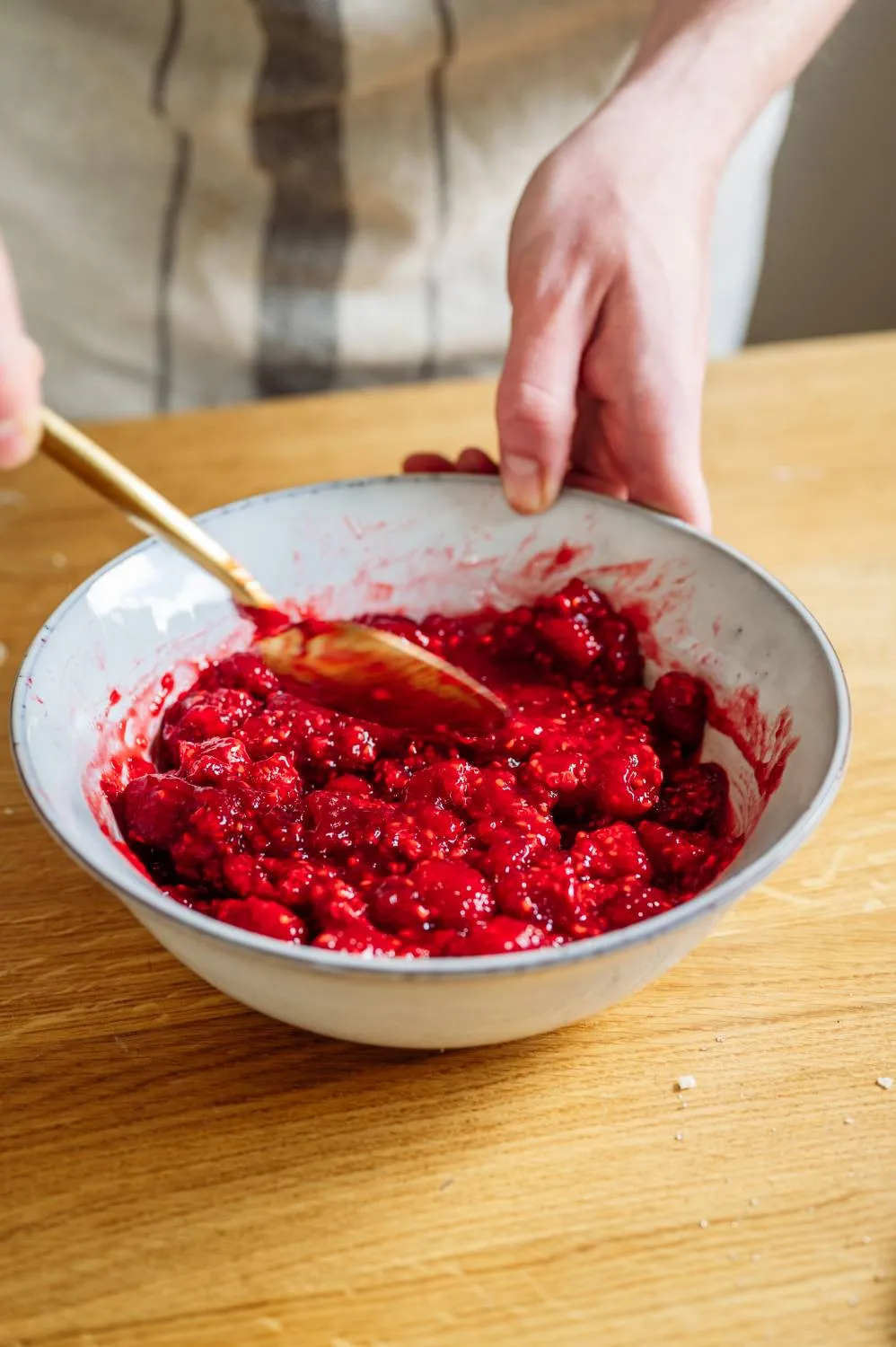Der Teig für den Streuselboden wird in eine Springform gedrückt, während Himbeeren bereitliegen