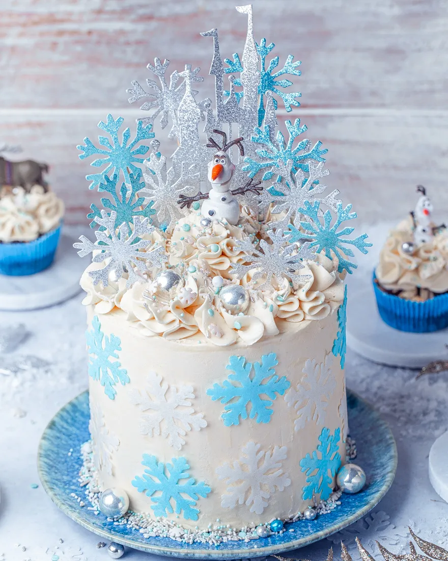 Detailaufnahme einer Eiskönigin-Torte, verziert mit Elsa- und Anna-Figuren und blauen Zuckerstreuseln.