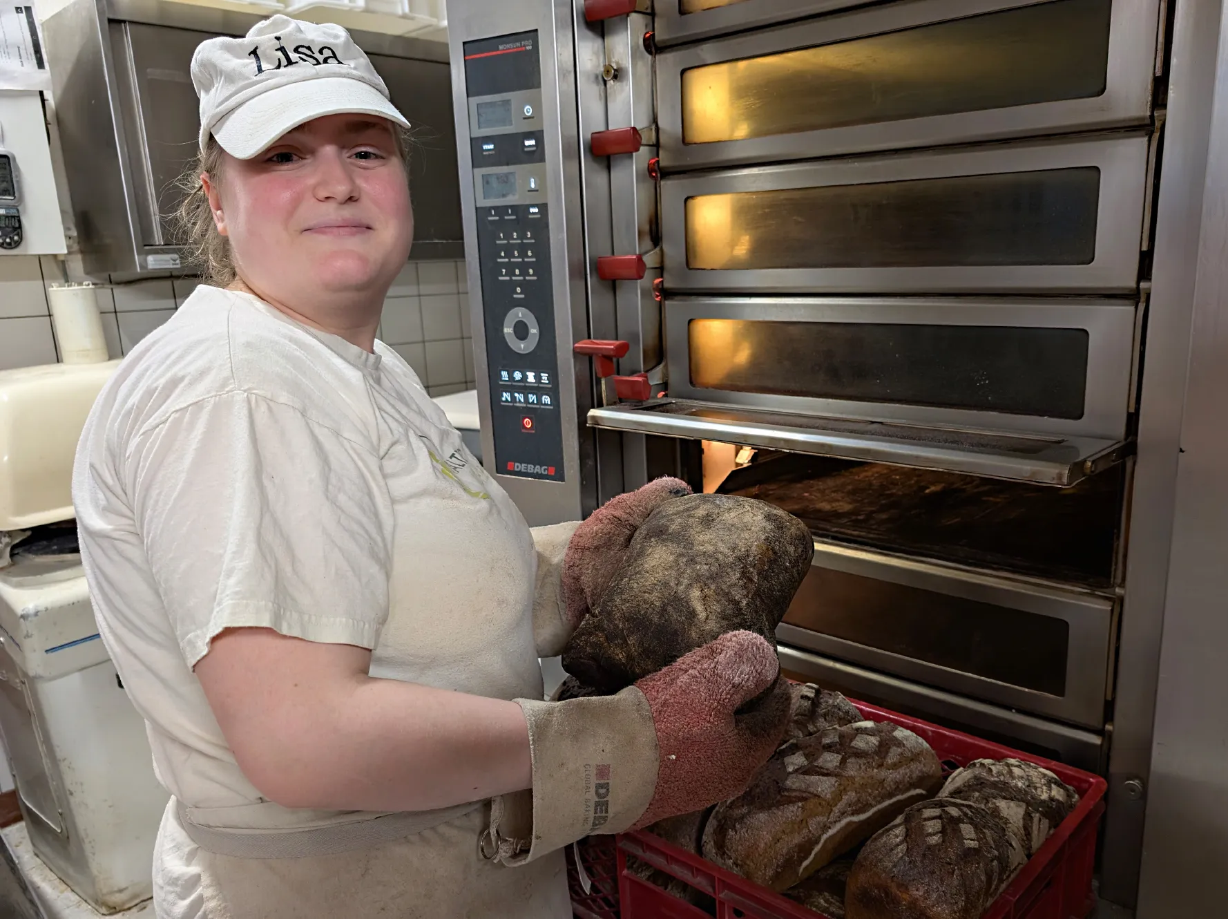 Die Bäckergesellin Lisa holt frisch gebackene, knusprige Brote aus einem großen Ofen