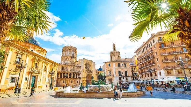 Die sonnenverwöhnte Strandpromenade von Valencia, gesäumt von Palmen und modernen Gebäuden, unter blauem Himmel.