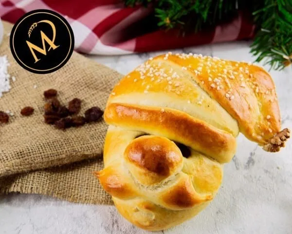 Drei festlich dekorierte Nikolaus-Köpfe aus süßem Hefeteig mit Mützen, Bärten und Rosinenaugen, bereit zum Backen