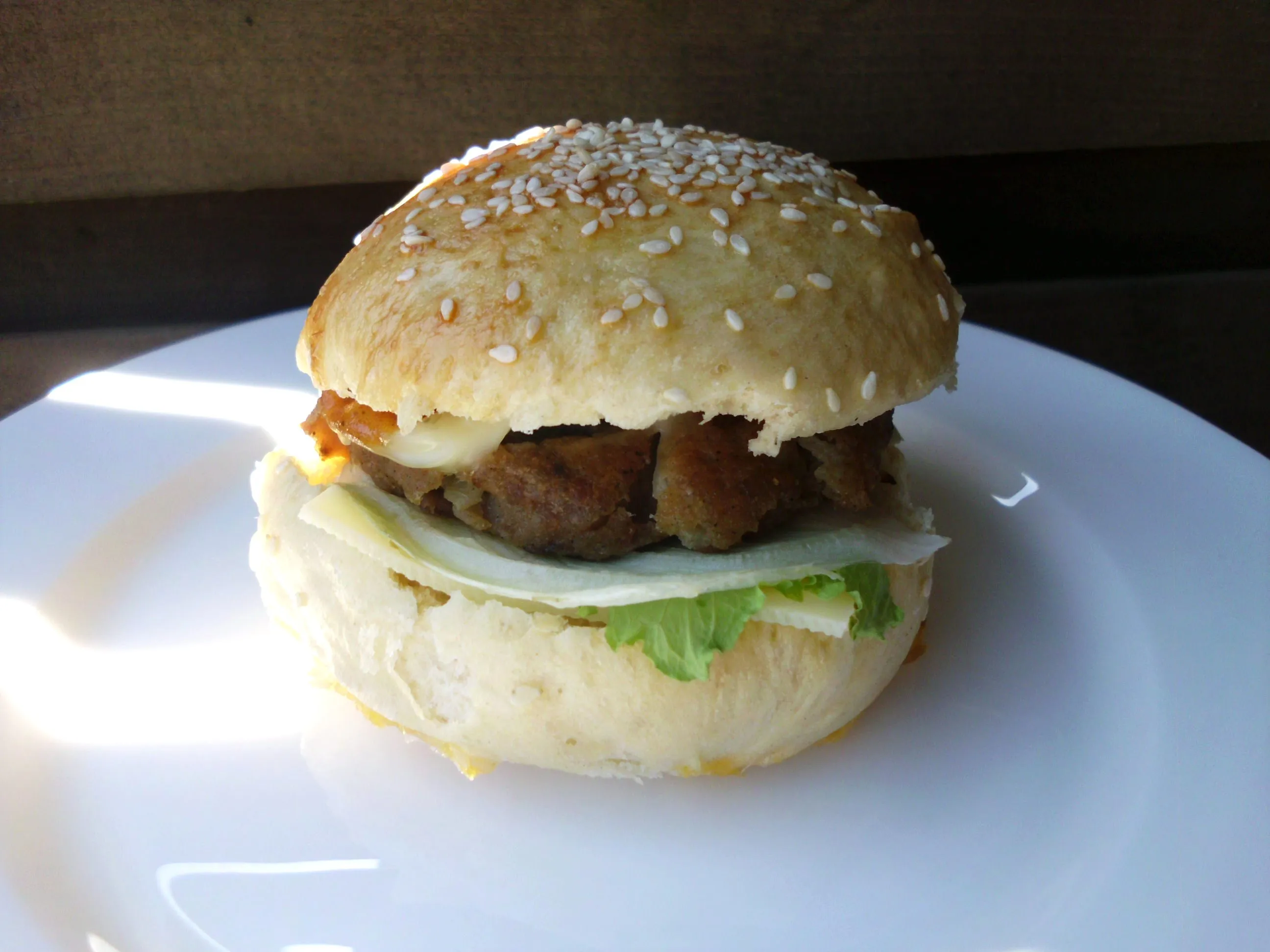 Drei frisch gebackene Hamburger Brötchen, eines davon aufgeschnitten mit einer Gabel daneben