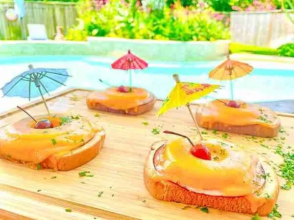 Drei frische Toast Hawaii mit Kirschen garniert auf einem Holzbrett.