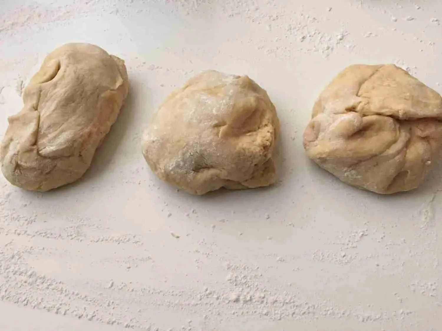 Drei gleich große Teigportionen liegen bereit auf einer bemehlten Arbeitsfläche