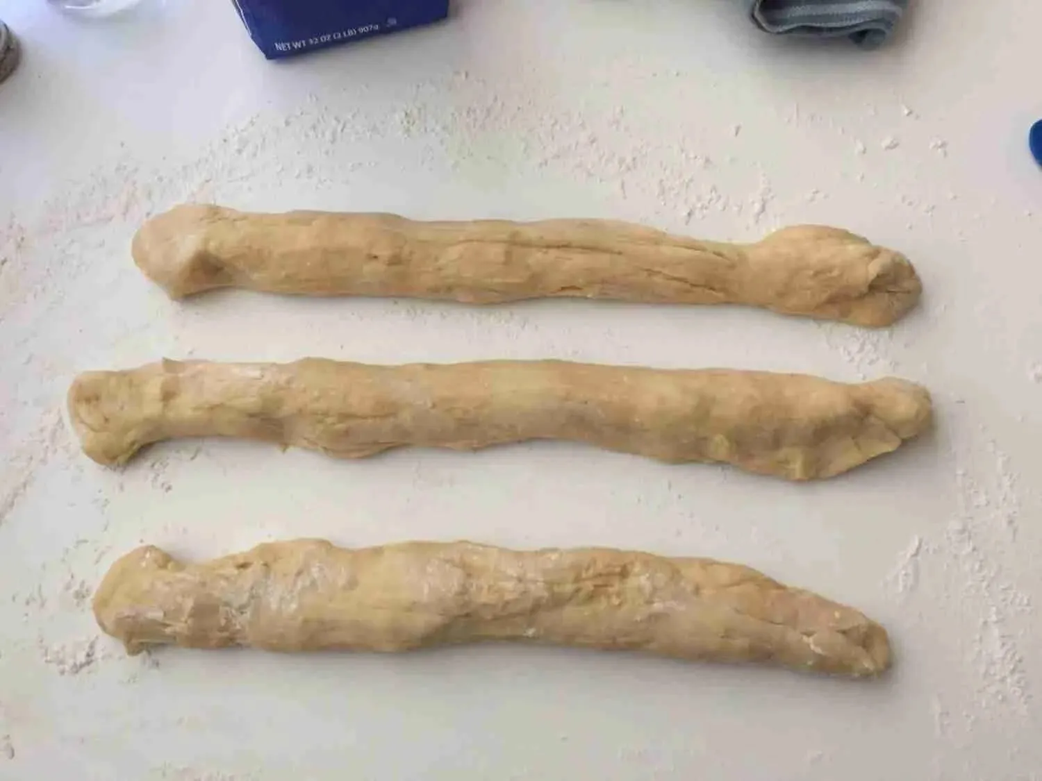 Drei lange, gleichmäßige Teigstränge, bereit zum kunstvollen Flechten eines Osterzopfs