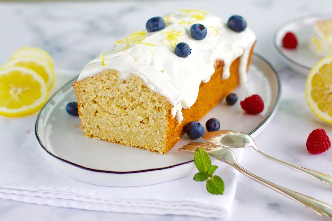 Drei Scheiben des saftigen Zitronen-Kokos-Kuchens auf einem Teller, dekoriert mit Joghurt-Topping