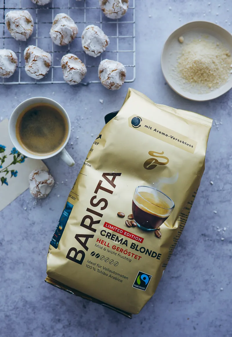 Drei Sizilianische Mandelgebäckstücke liegen auf einer Servierplatte neben einer Tasse Kaffee