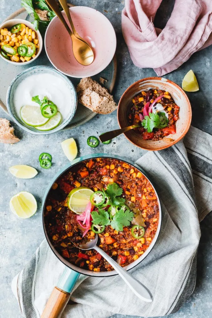 Ein angerichtetes One-Pot Quinoa Chili in einer Schale, reichlich garniert mit frischen Toppings und Limettenspalten.