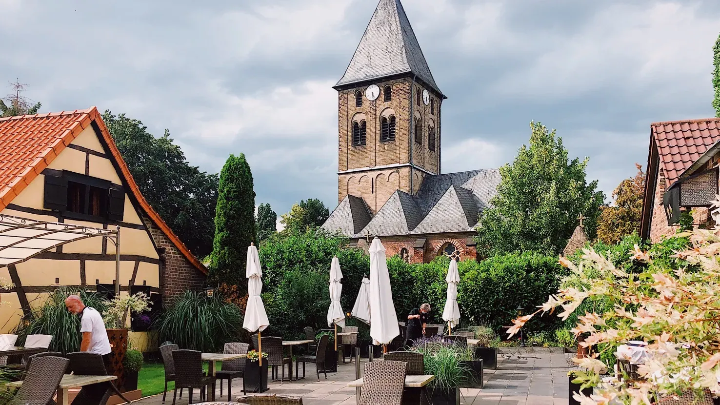 Ein Aperol Spritz auf einem Holztisch mit Blick auf eine malerische Kirche im Biergarten von Goebels