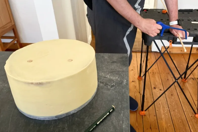 Ein Bild, das den Vorgang des Zuschneidens eines Tortendübels zeigt, bevor er in die Torte gesteckt wird, um Stabilität zu gewährleisten.