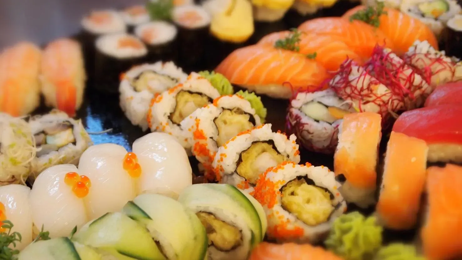 Ein Blick in eine belebte Restaurantküche, in der Köche frisches Sushi zubereiten, mit Dampf und geschäftigem Treiben.