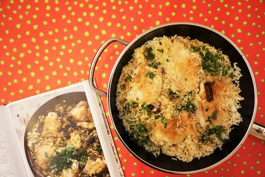 Ein dampfendes Gericht mit Hähnchenstücken, karamellisierten Zwiebeln und duftendem Kardamomreis.