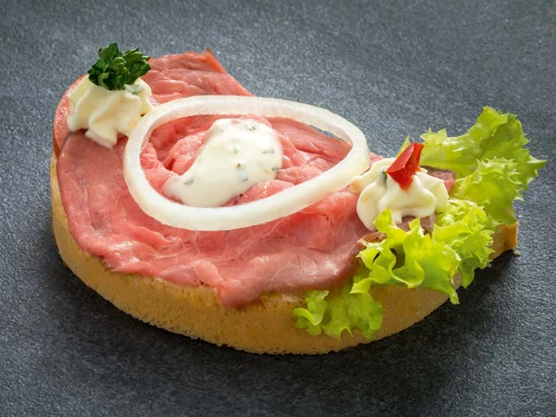 Ein einzelnes Brötchen belegt mit saftigem rosa gebratenem Roastbeef.